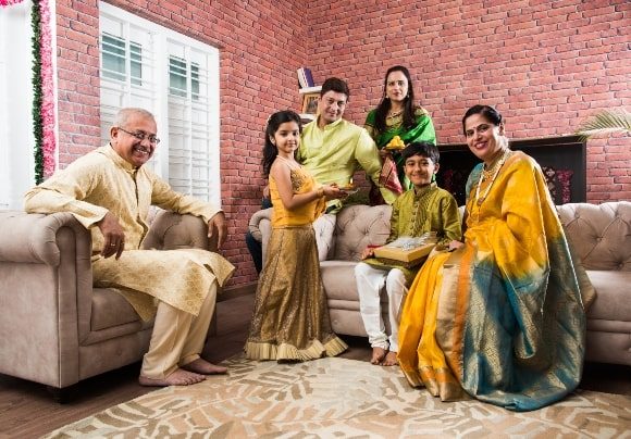 indian-family-celebrating-raksha-bandhan-rakhi-festival-home-while-wearing-traditional-cloths-sitting-sofa (1)-min